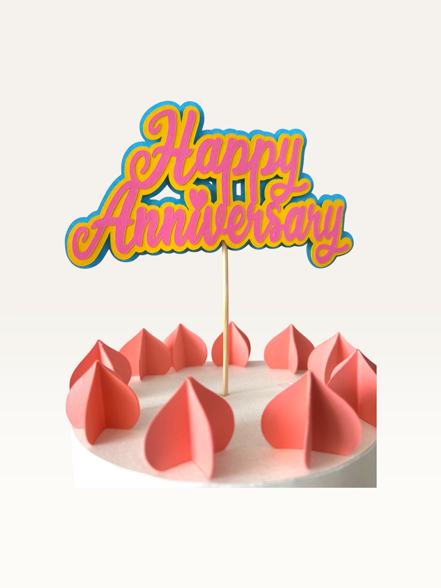 Paper Party Studio layered script Happy Anniversary cake topper in pink and blue on a wooden pick.