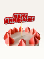 Paper Party Studio handmade red and white Happy Anniversary cake topper with heart cut-outs on a wooden pick