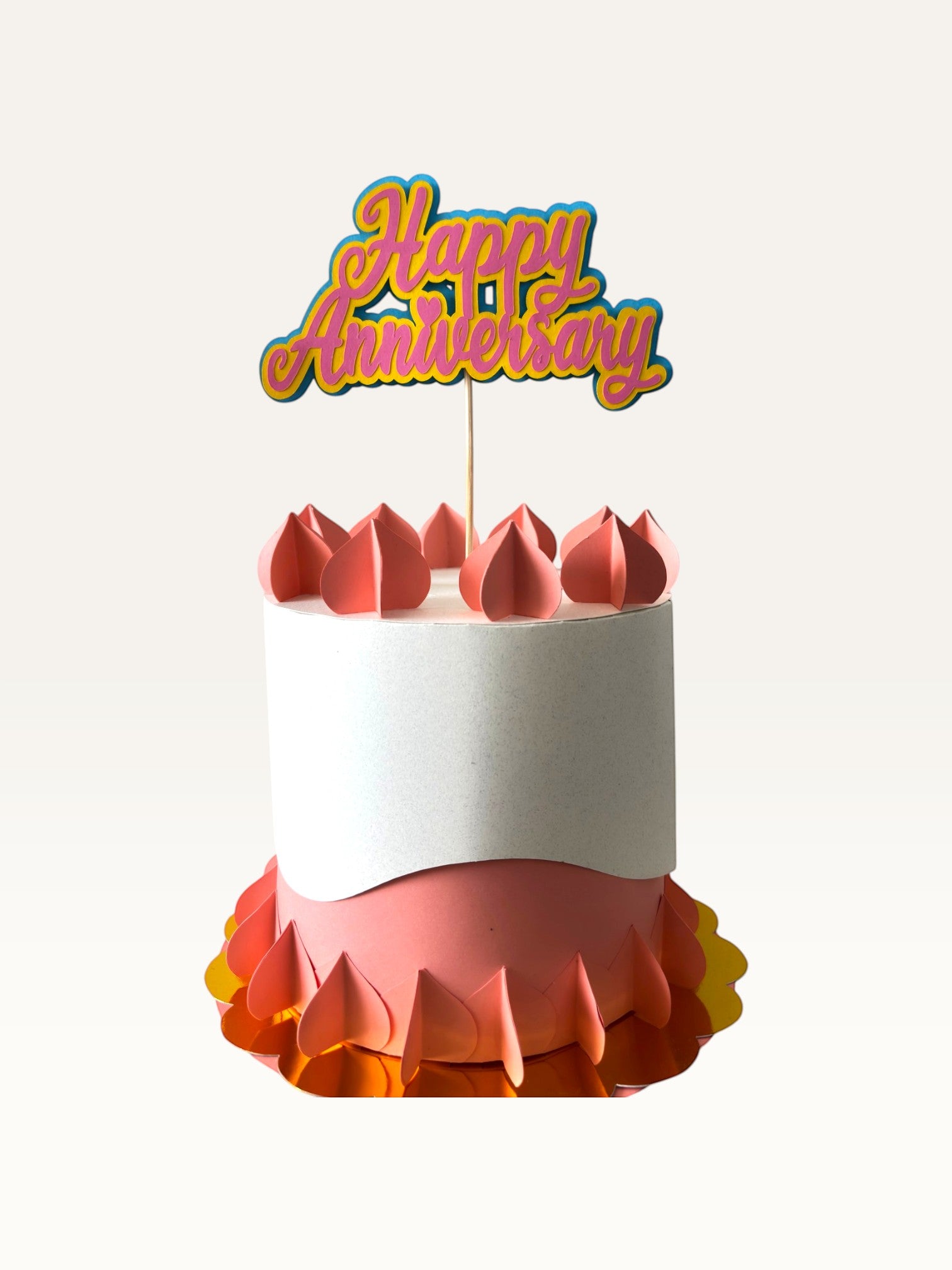 Paper Party Studio layered script Happy Anniversary cake topper in pink and yellow on a decorative paper cake