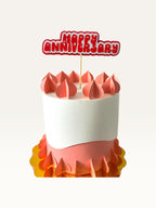 Paper Party Studio Happy Anniversary cake topper with red bubble letters and heart cut-outs on a decorative cake.