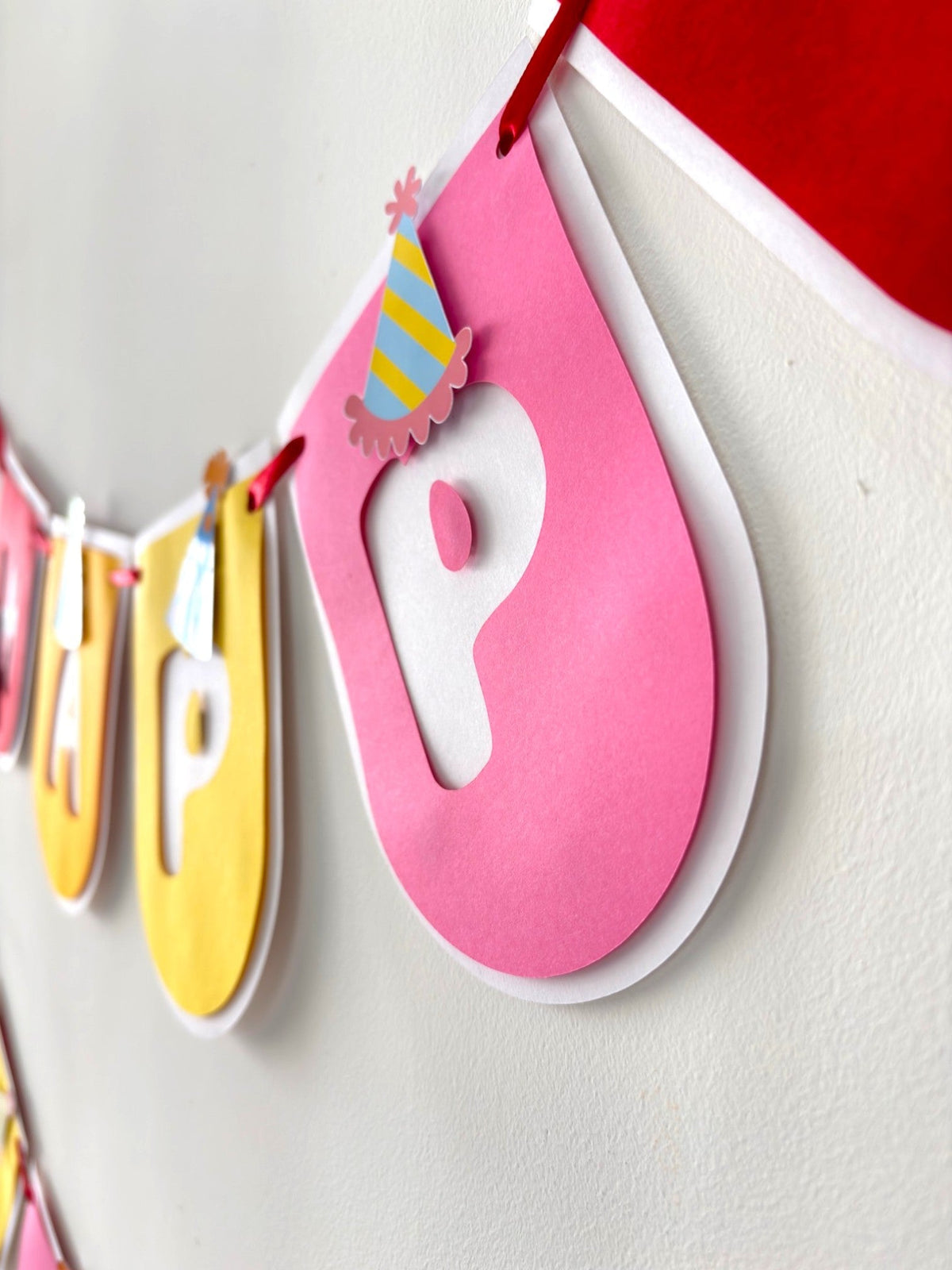 Paper Party Studio Happy Birthday banner featuring rounded pink and yellow flags with layered party hat accents