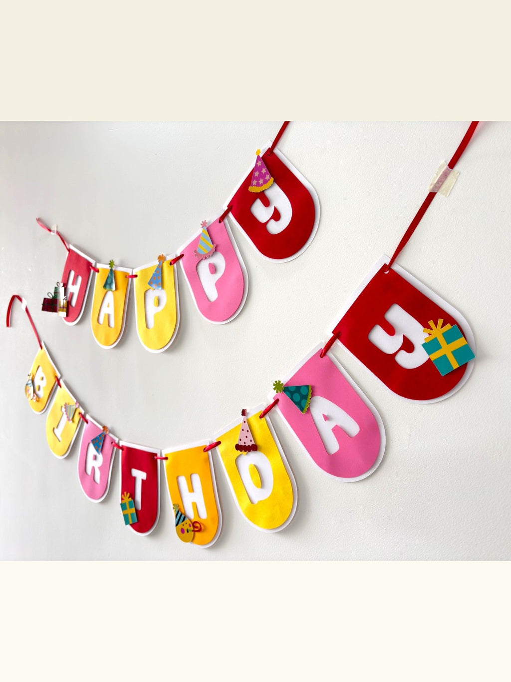Paper Party Studio Happy Birthday banner with multicoloured rounded flags, party hats, and gift accents on two strings
