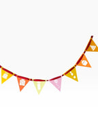 Paper Party Studio birthday pennant bunting with cake, gift, balloon cut-outs on yellow, orange, pink flags strung on red ribbon.