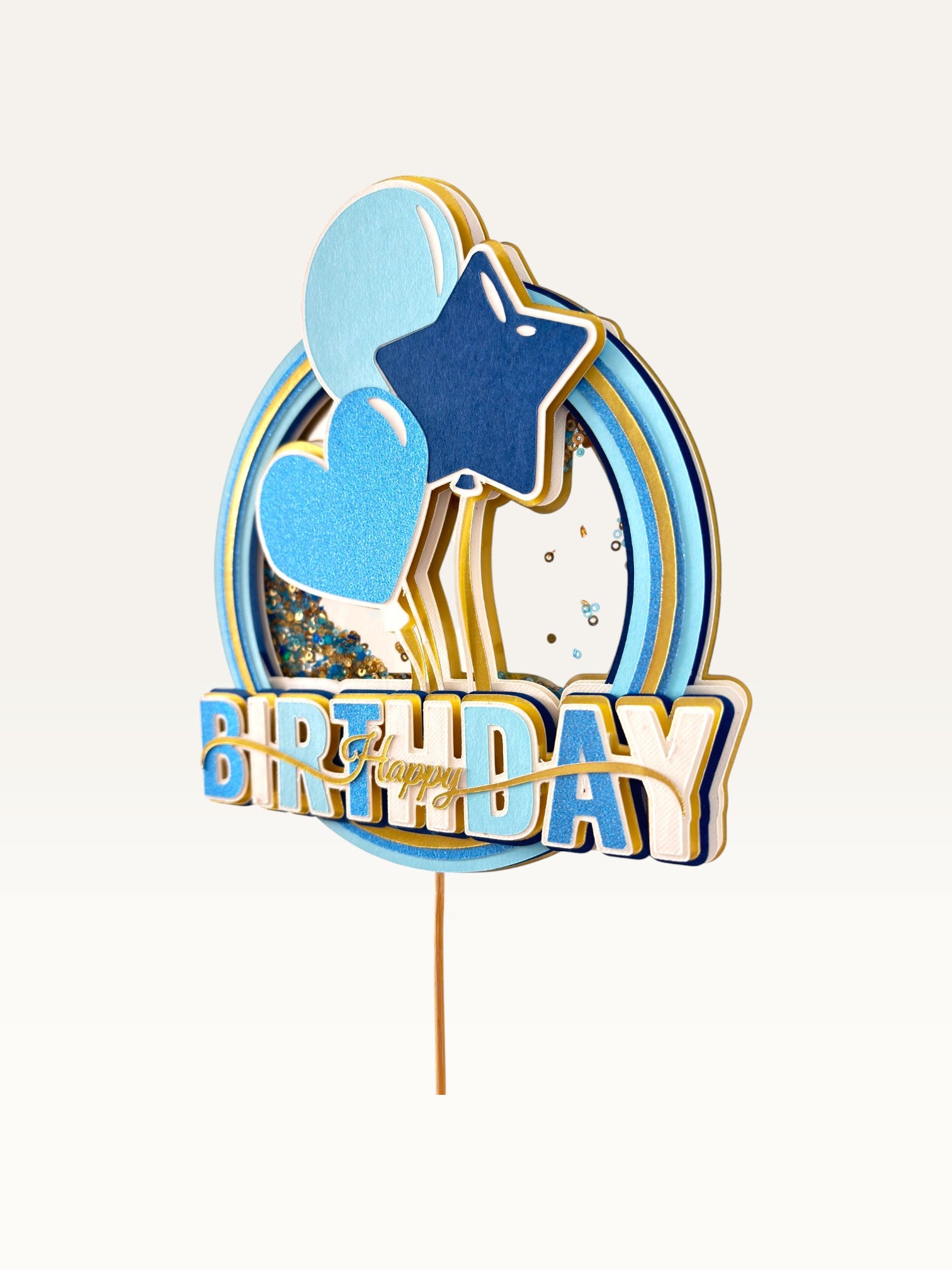 Paper Party Studio blue and gold Happy Birthday shaker cake topper with glitter, sequins, and balloon decorations.