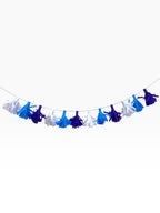 Paper Party Studio paper tassel garland in blue, purple, and white hanging on a string for birthday party decor.