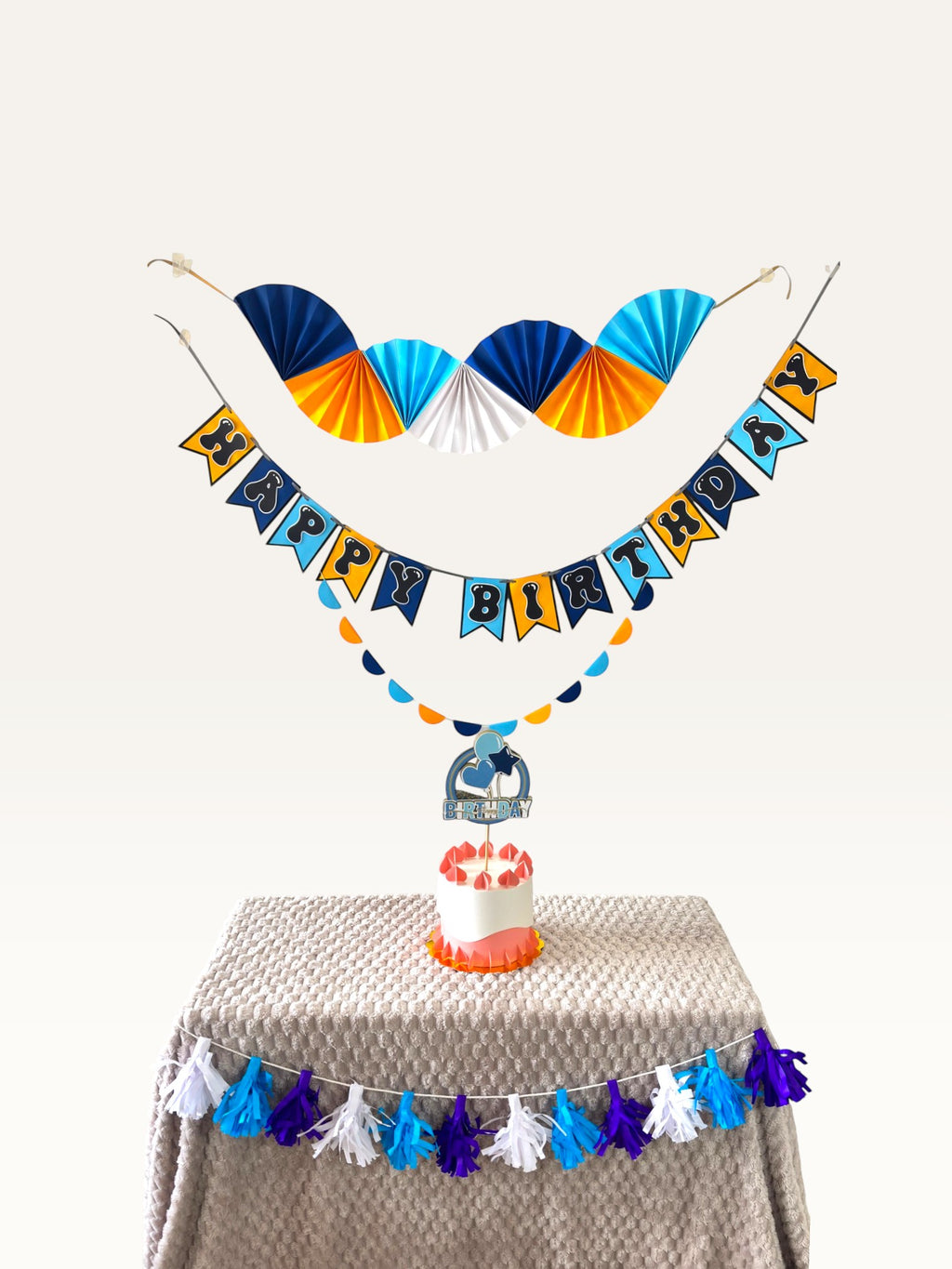 Paper Party Studio blue and yellow birthday decoration set with paper fans, Happy Birthday banner, and cake topper.