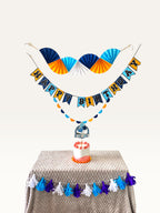 Paper Party Studio blue and yellow birthday decoration set with paper fans, Happy Birthday banner, and cake topper.
