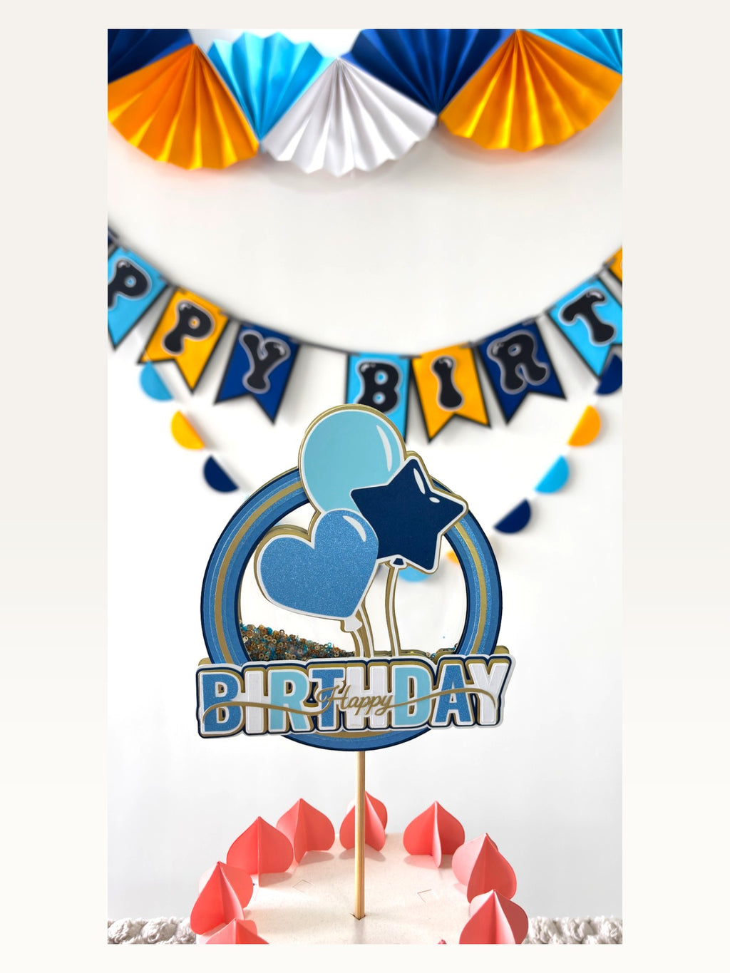 Paper Party Studio blue and yellow birthday decoration set including a cake topper, banner, and paper fan backdrop.