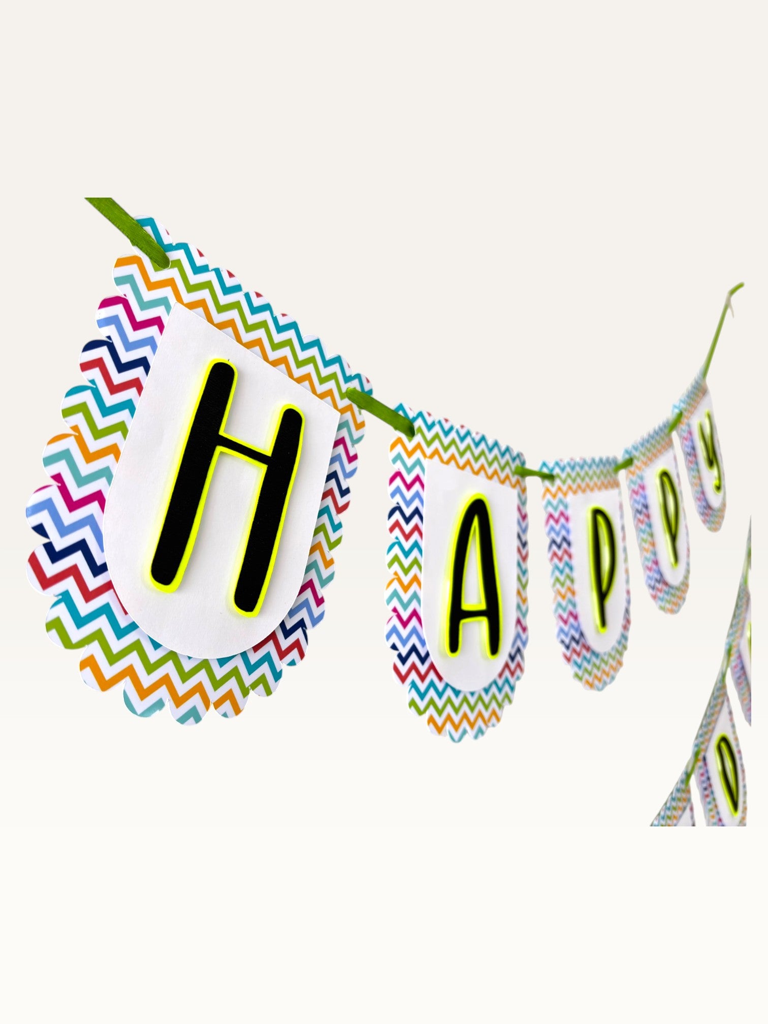Paper Party Studio Happy Birthday banner with white scalloped paper flags, multicolour chevron border, and black text.