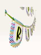 Paper Party Studio Happy Birthday banner with scalloped white tags, multicolour chevron borders, and black letters.