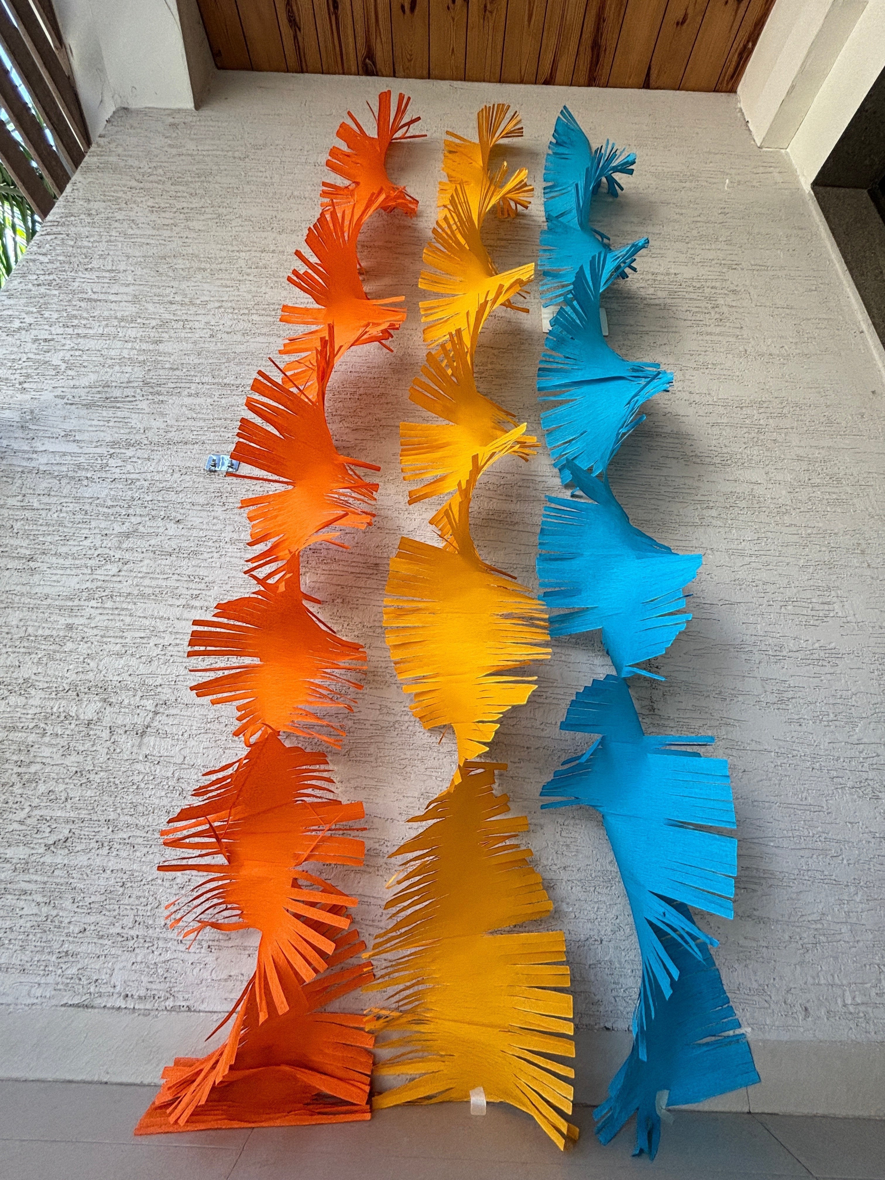 Paper Party Studio orange, yellow, and blue crepe paper fringe streamers hanging vertically.