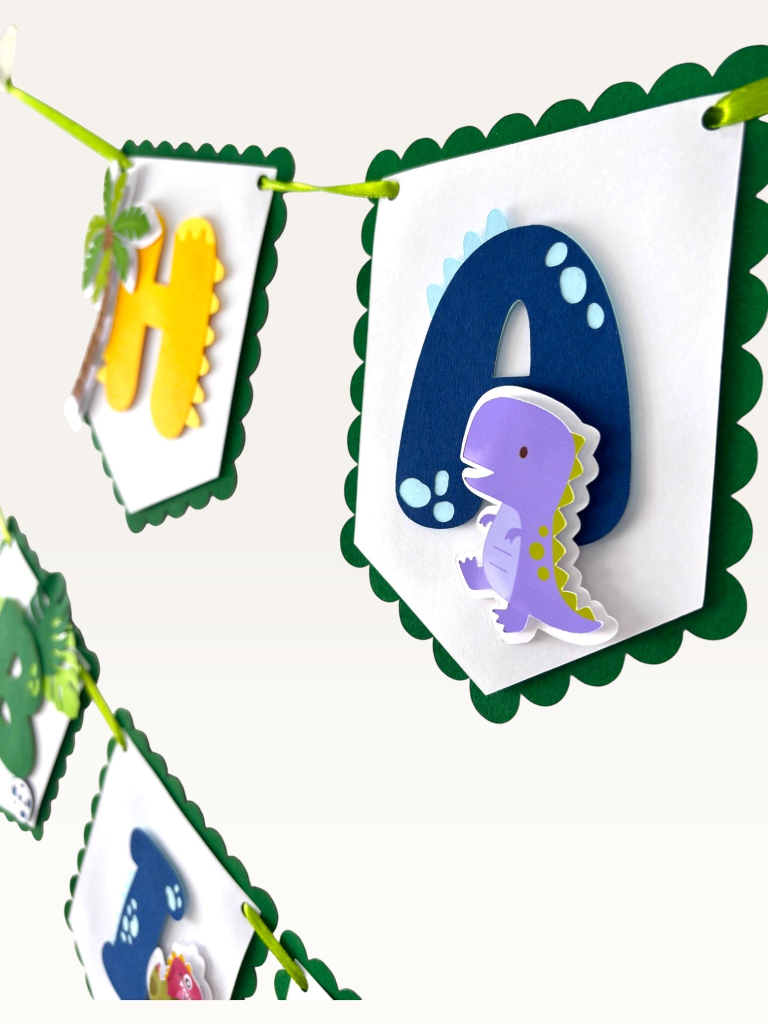 Paper Party Studio dinosaur happy birthday banner with scalloped white flags, green borders, and layered dino letters.