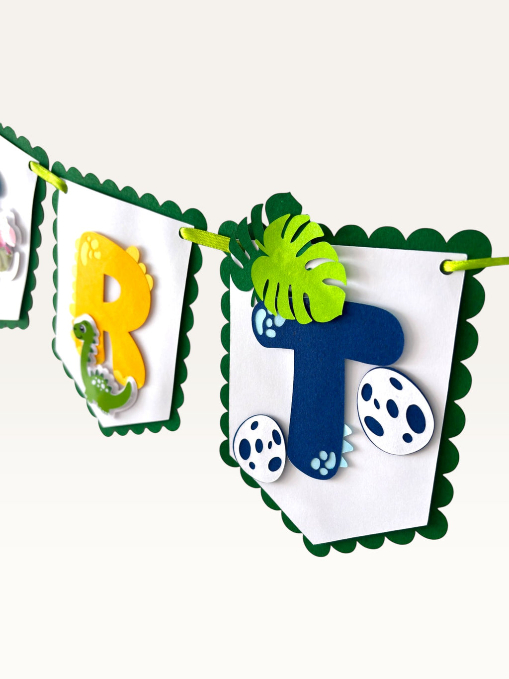 Paper Party Studio dinosaur birthday banner with scalloped white cardstock flags, green borders, and jungle decor.