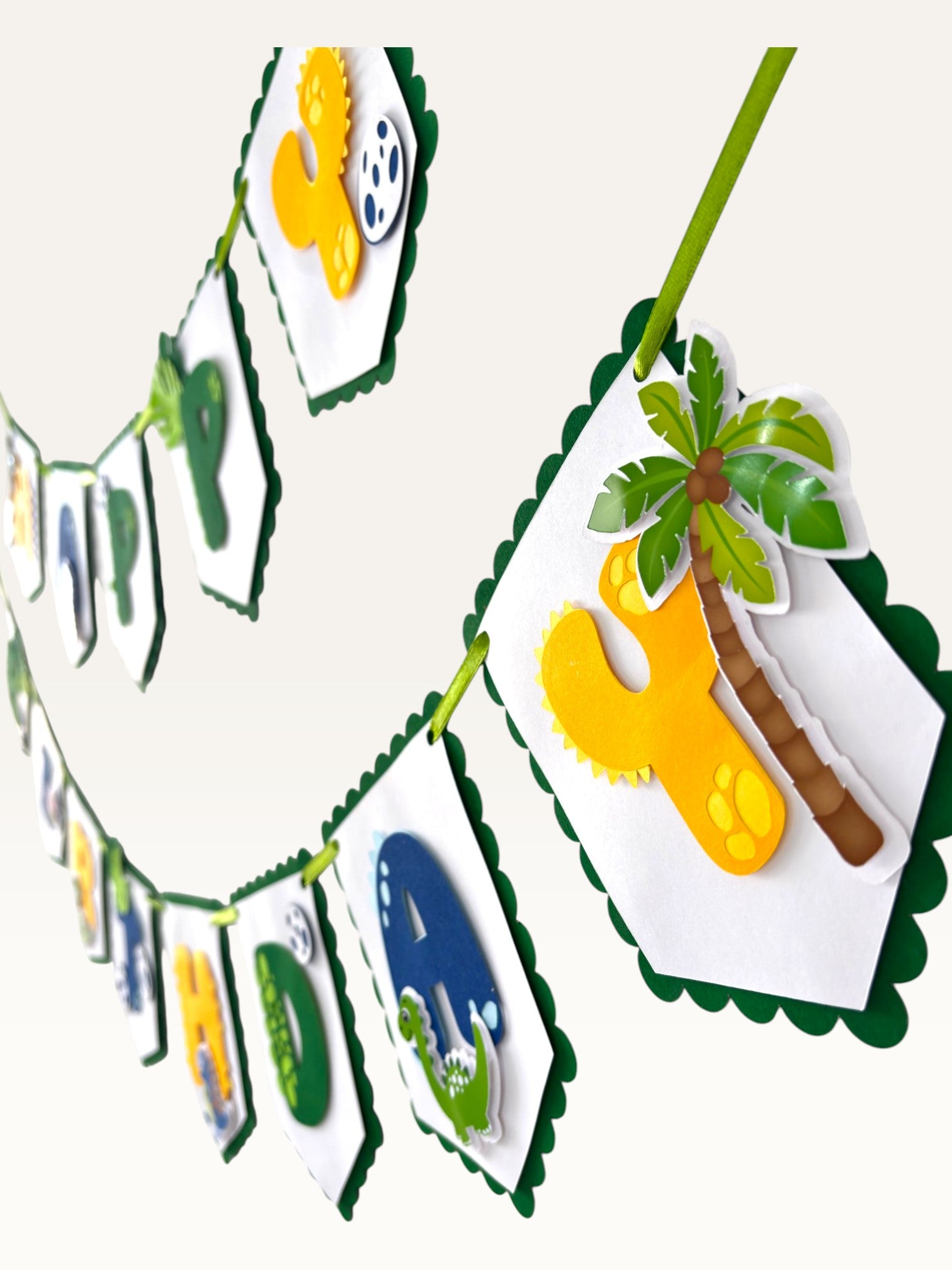 Paper Party Studio dinosaur happy birthday banner with scalloped white flags, jungle leaves, and palm tree decorations.