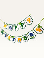 Paper Party Studio dinosaur Happy Birthday banner with scalloped white flags, jungle motifs, and colorful letters.