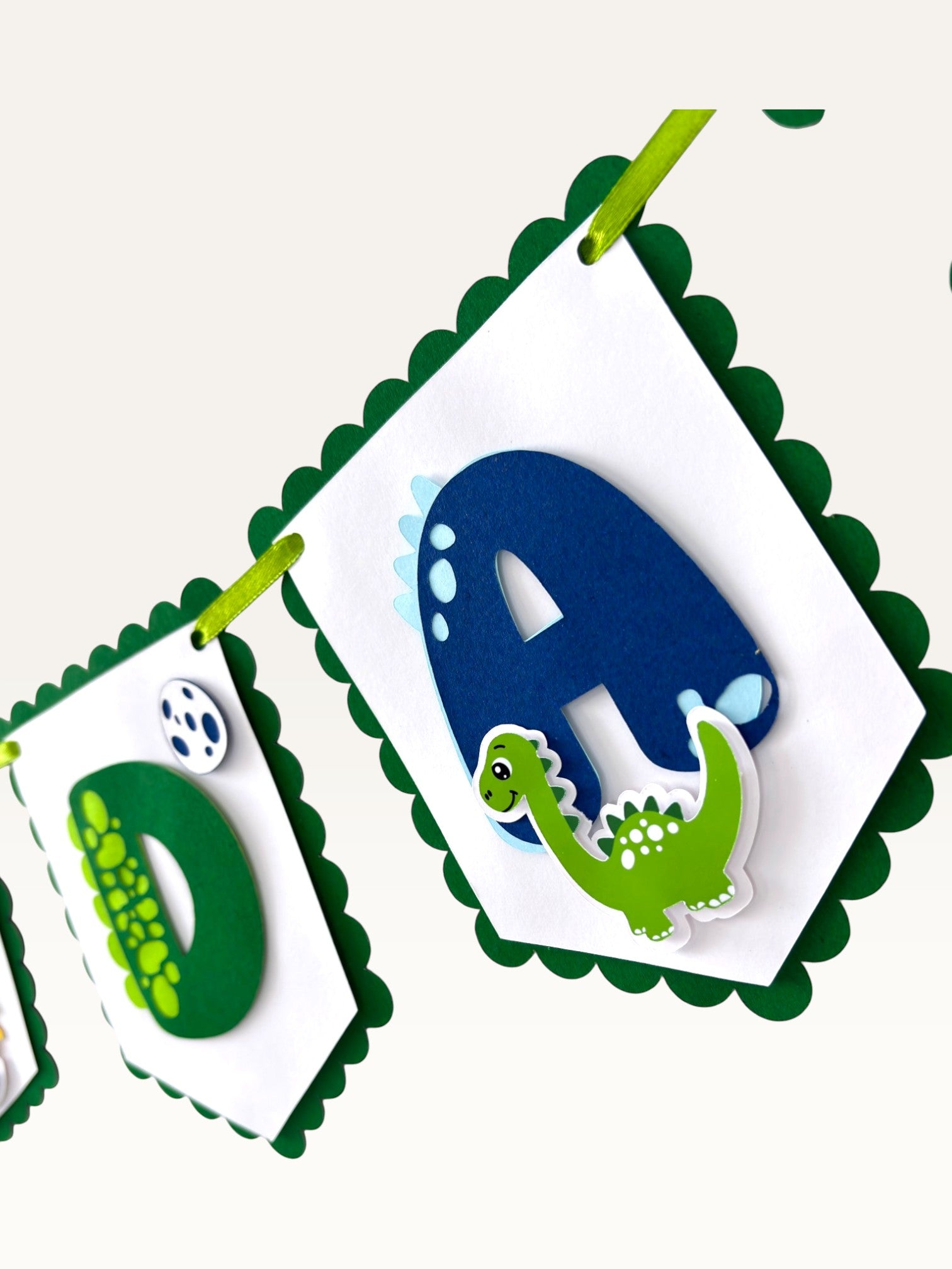 Paper Party Studio dinosaur birthday banner with scalloped white flags, green borders, and layered cardstock letters