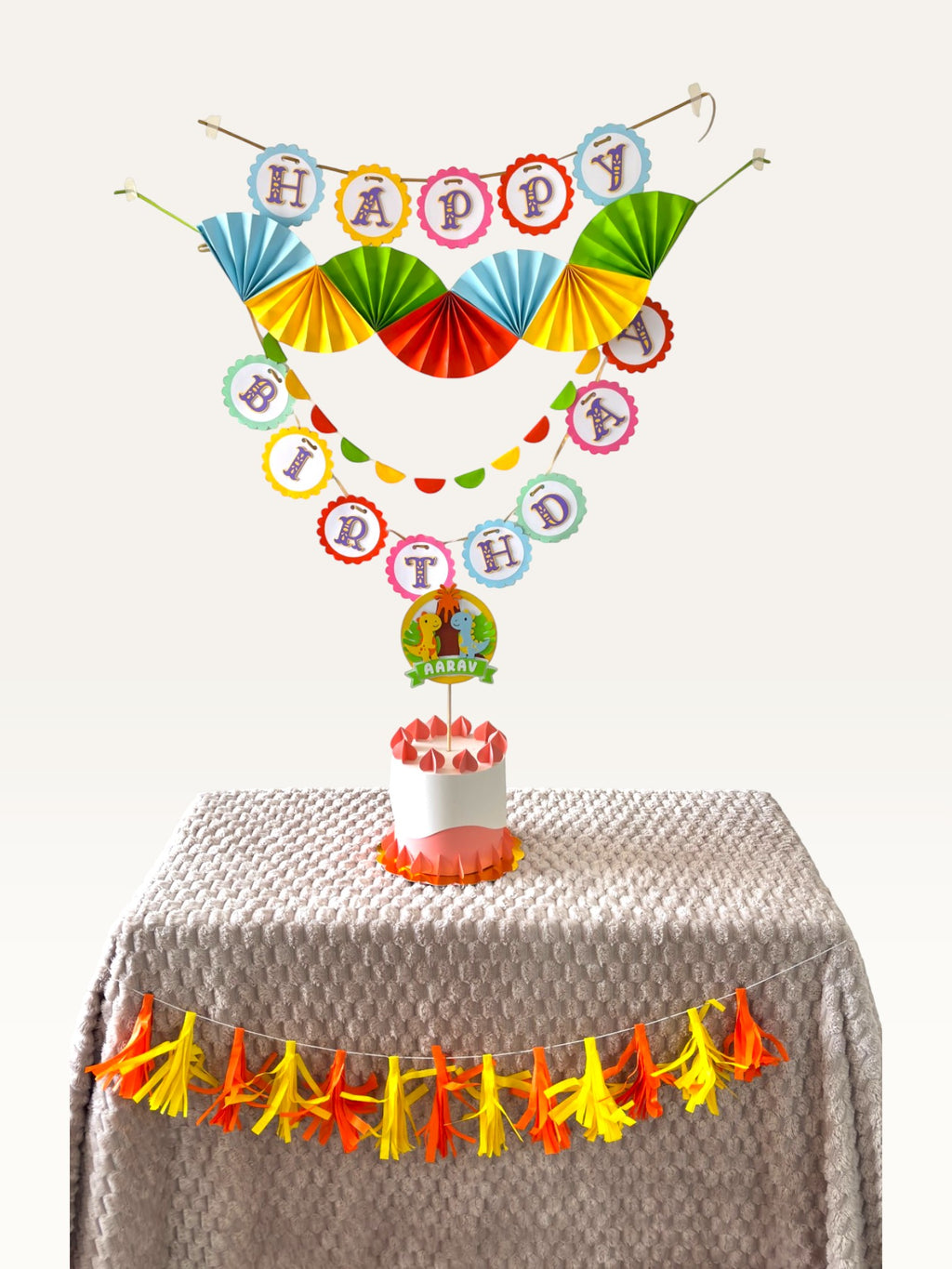 Paper Party Studio personalised dinosaur birthday decoration set with colourful paper fans, banners, and cake topper.