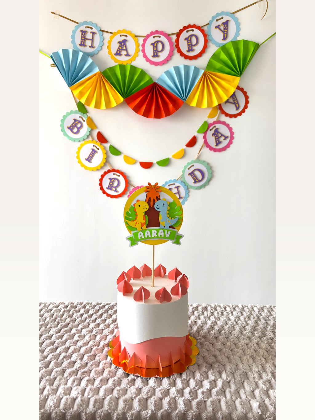 Paper Party Studio dinosaur birthday party decoration set with personalised cake topper, banner, and paper fans.