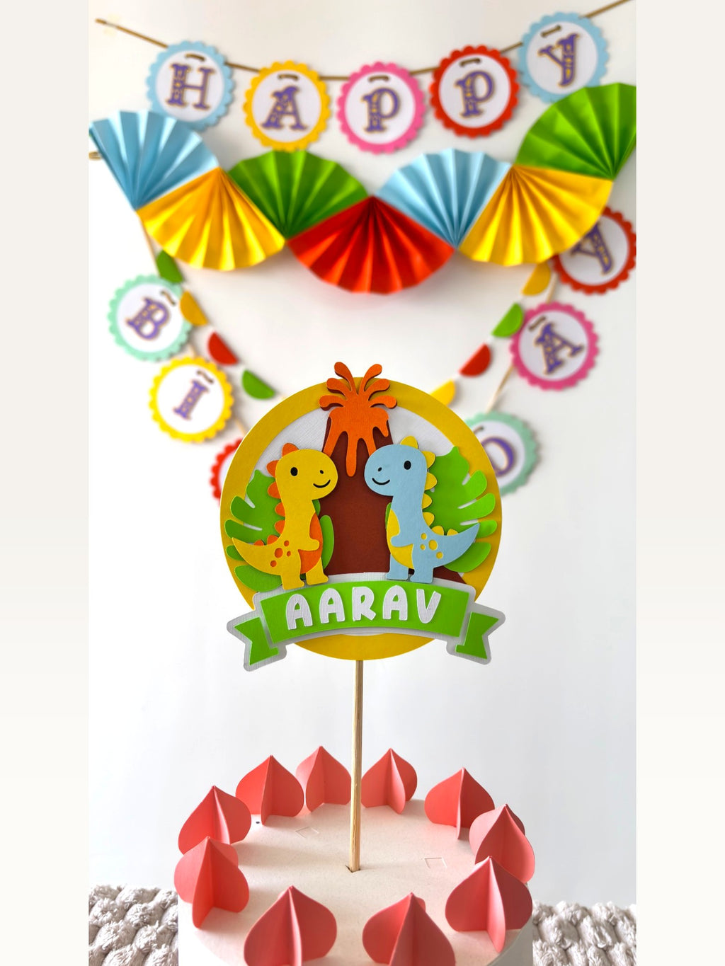 Paper Party Studio personalised dinosaur cake topper with a Happy Birthday banner and colourful paper party decorations.