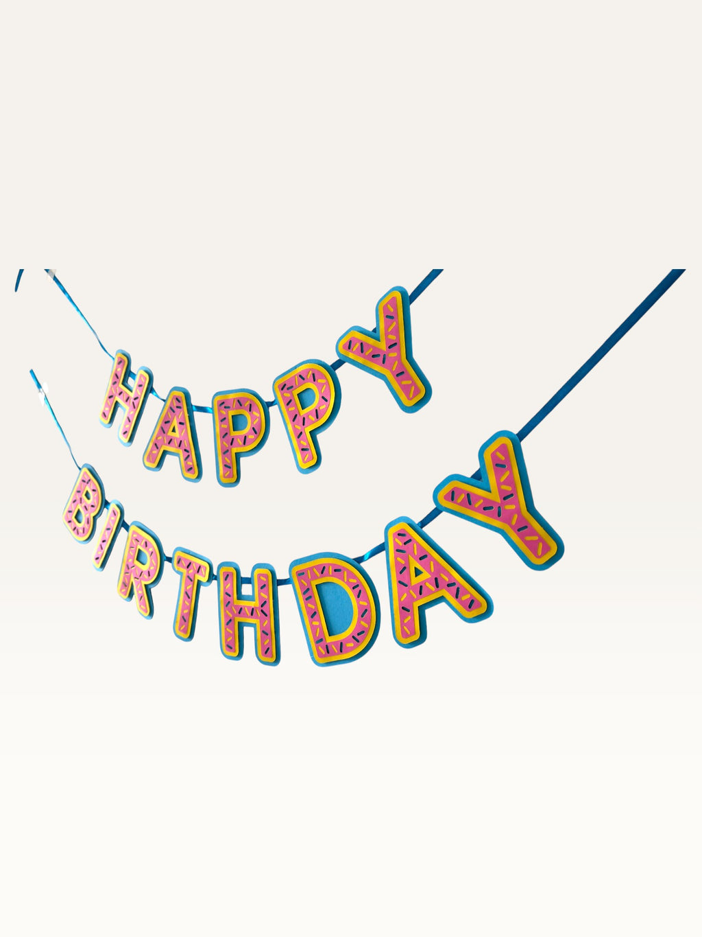 Paper Party Studio pink donut-glaze Happy Birthday banner with candy sprinkle details on a blue string.