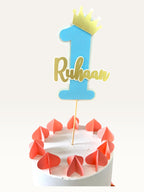 Paper Party Studio personalized blue number one cake topper with gold crown and name on a decorative cake