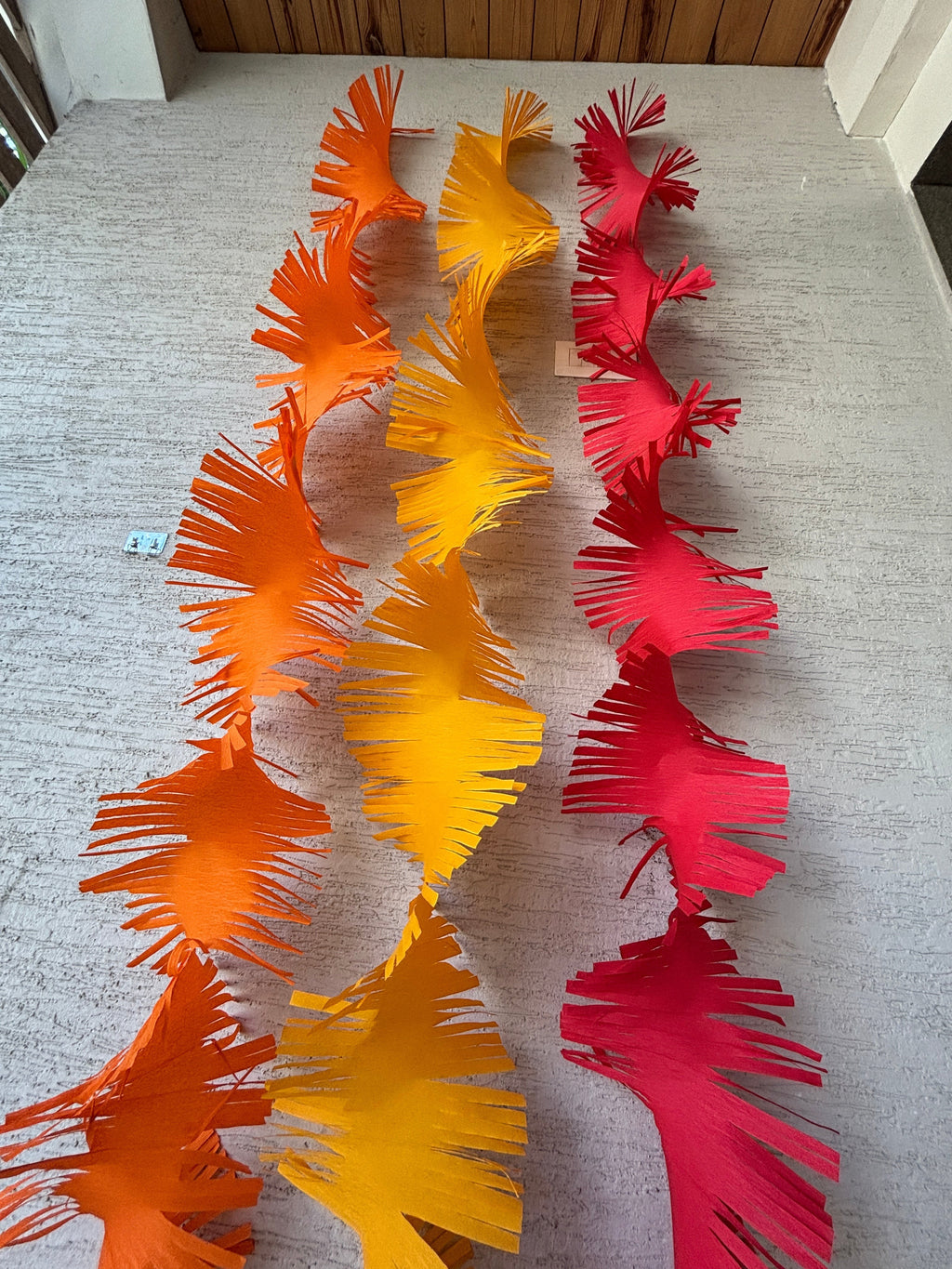 Paper Party Studio orange, yellow, and red crepe paper fringe streamers hanging vertically.
