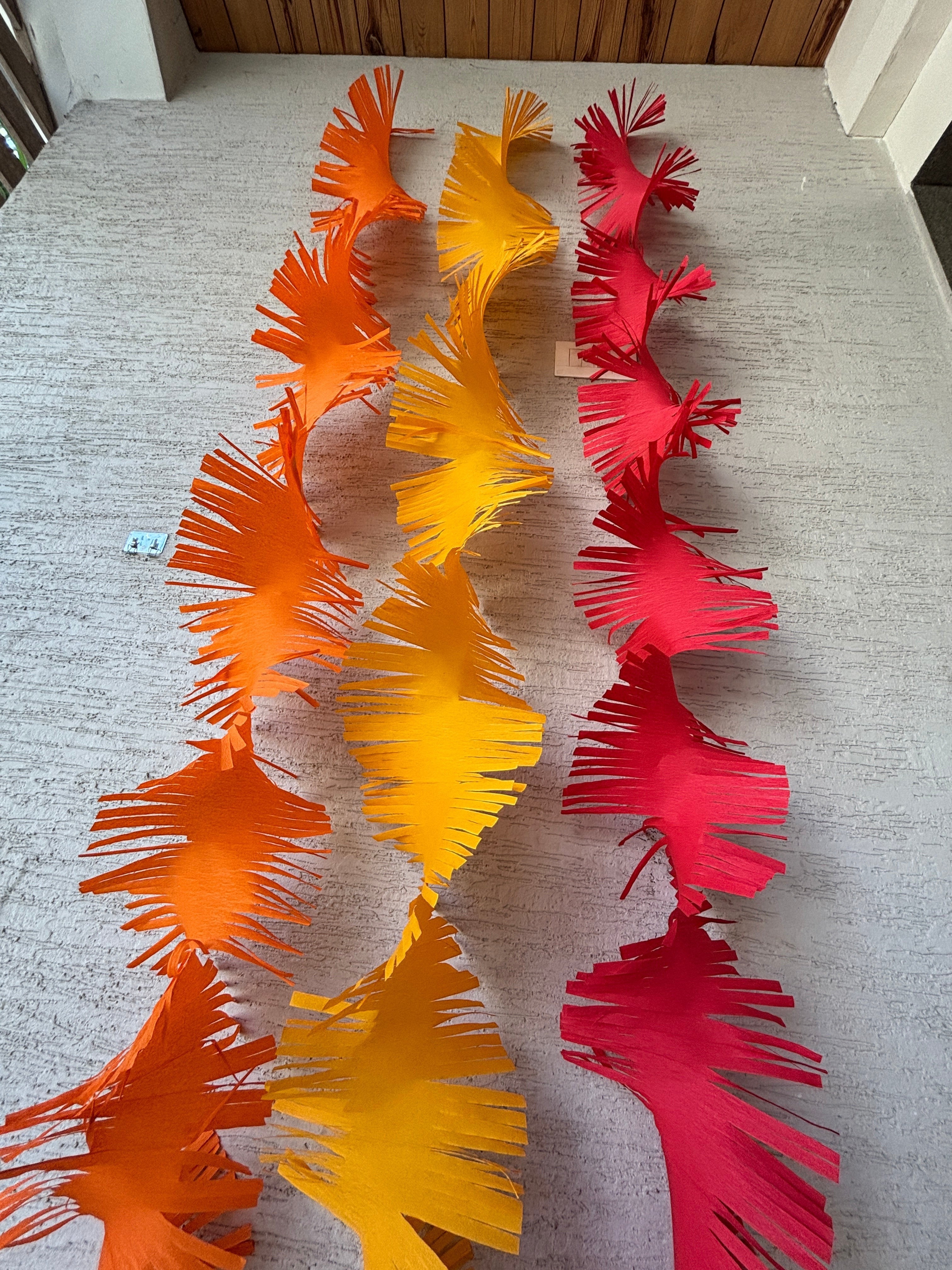 Paper Party Studio orange, yellow, and red crepe paper fringe streamers hanging vertically.