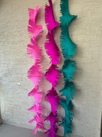Paper Party Studio pink and teal paper fringe streamers hanging vertically against a textured wall.