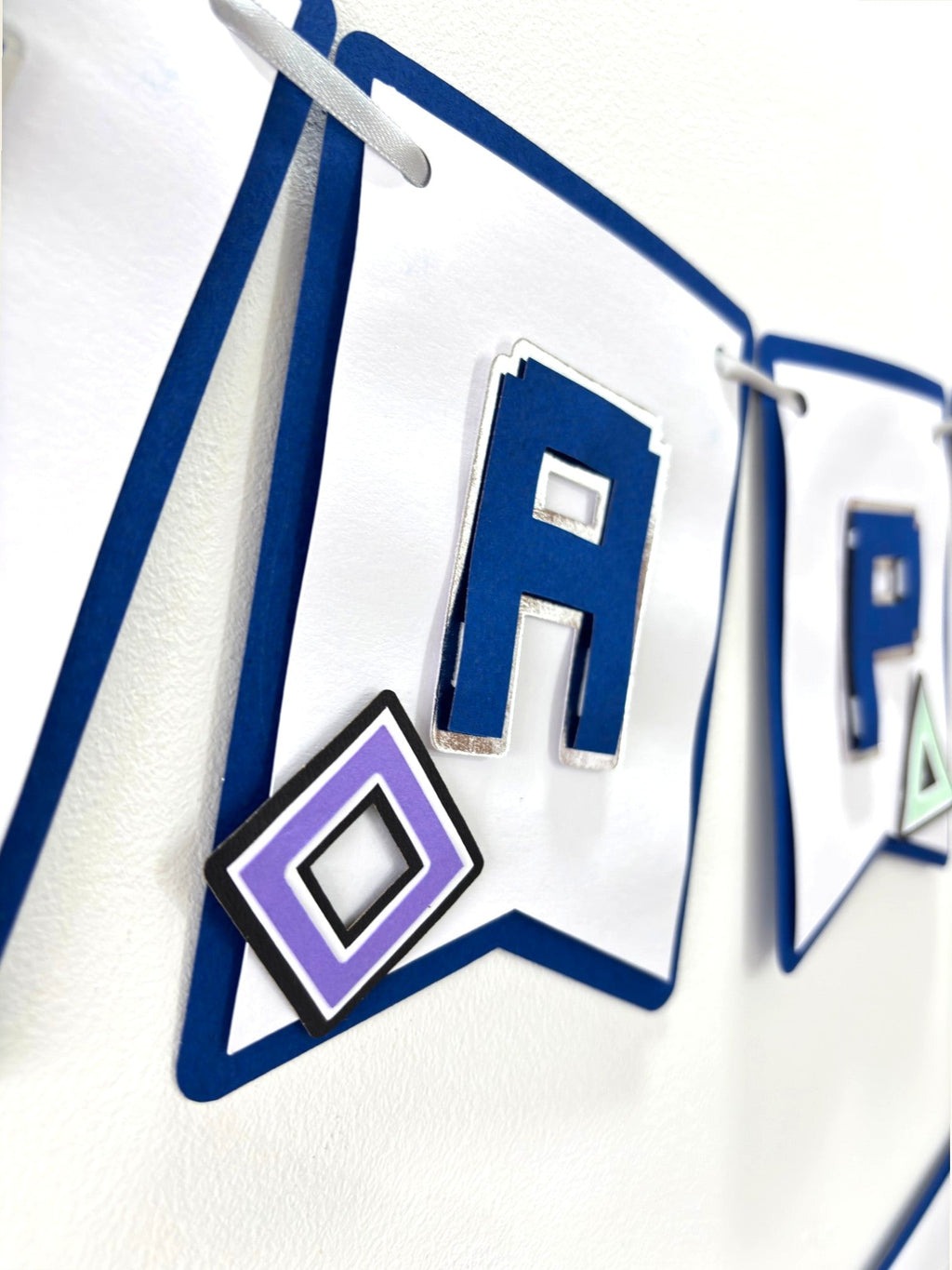 Paper Party Studio gaming birthday banner with white flags, navy letters, silver edges, and purple geometric icons.