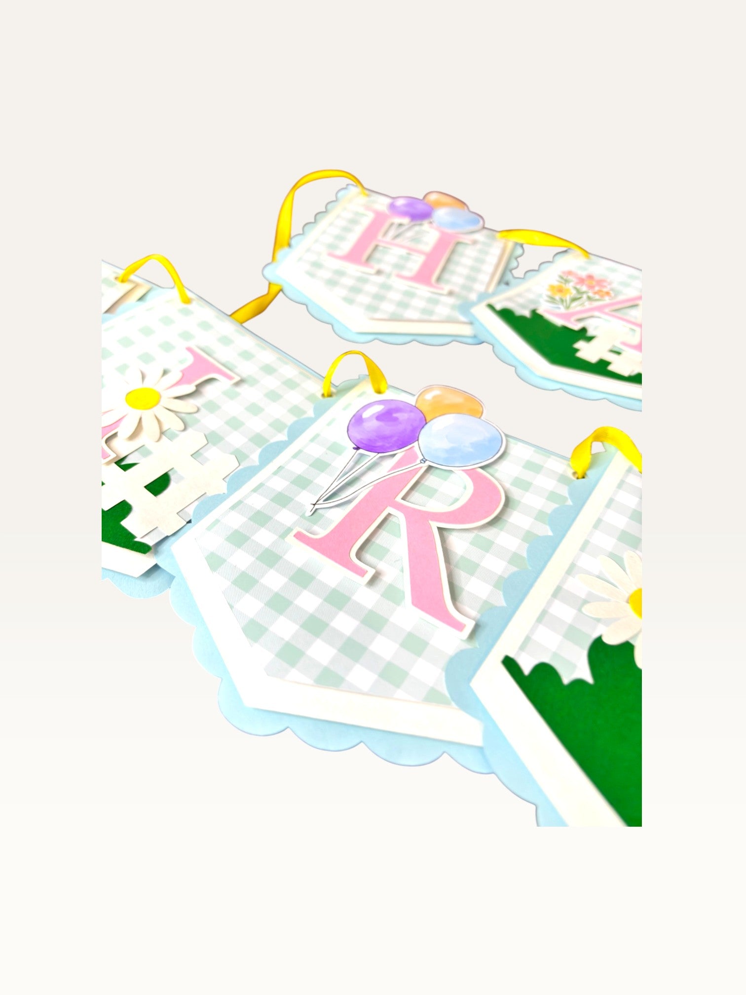 Paper Party Studio pastel blue gingham birthday banner with pink letters, balloons, and daisy floral accents.