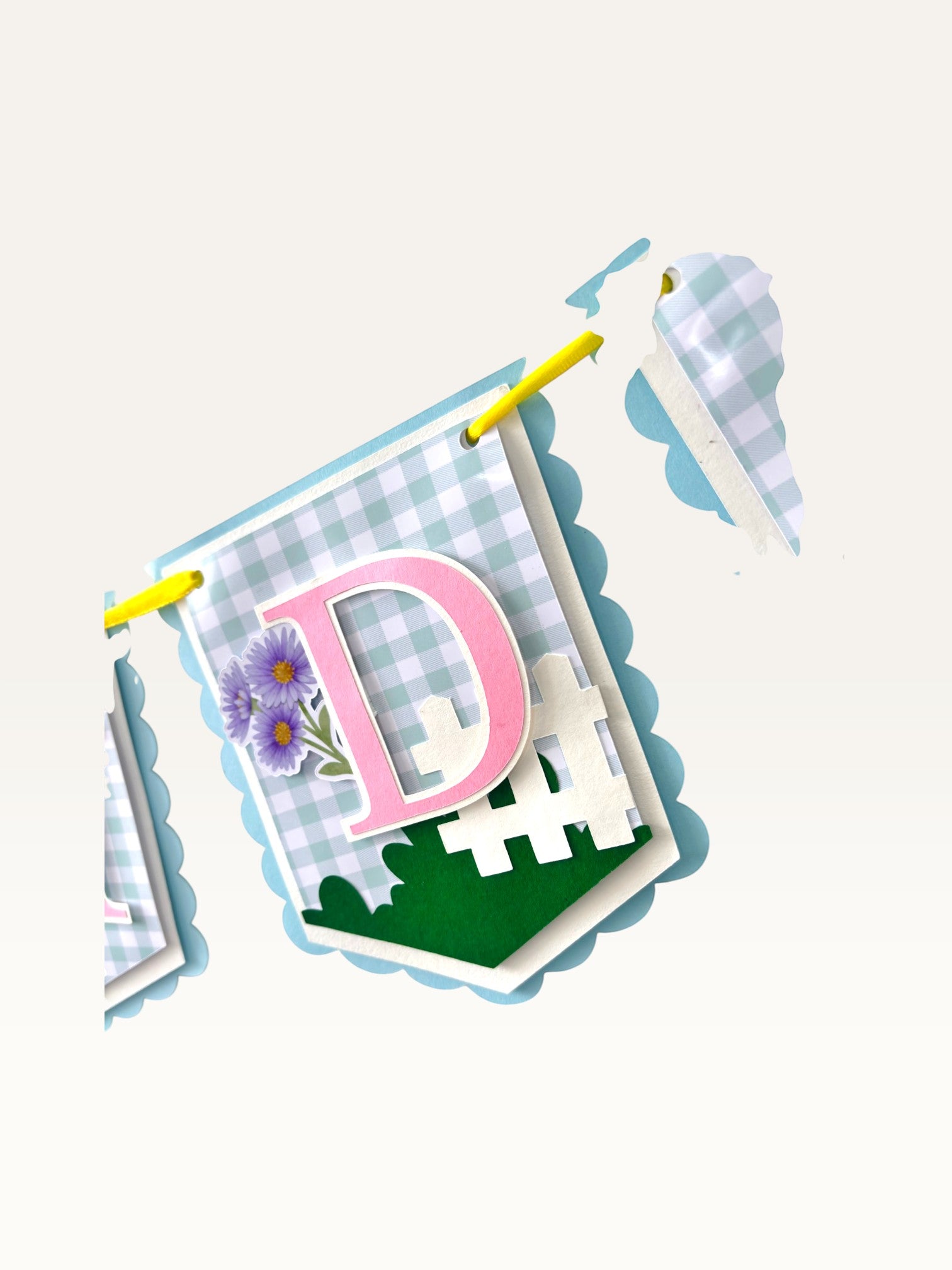 Paper Party Studio blue gingham birthday banner flag with pink letter D, white picket fence, and purple daisies