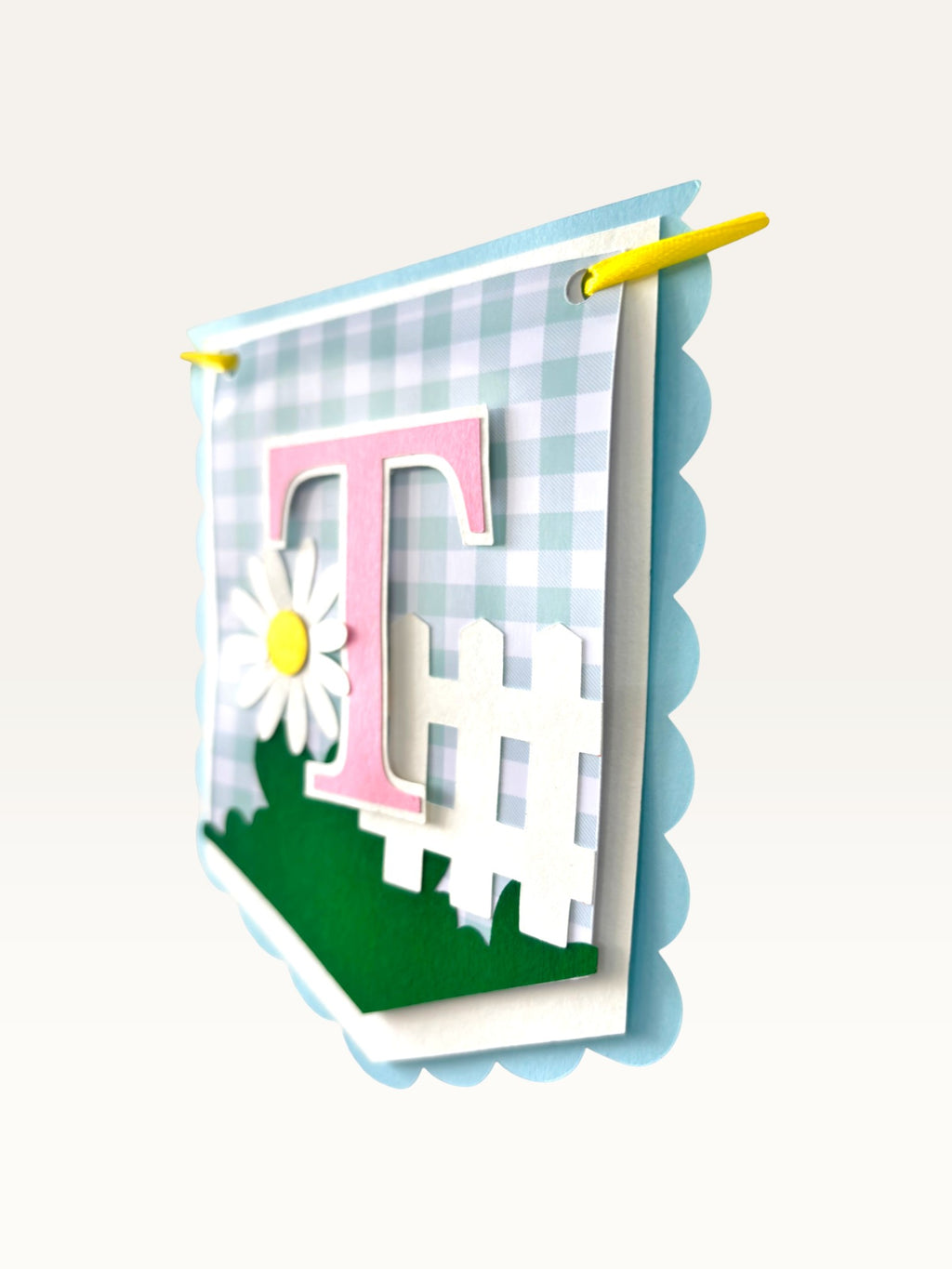 Paper Party Studio Gingham Garden birthday banner flag featuring a pink letter T, white picket fence, and daisy.