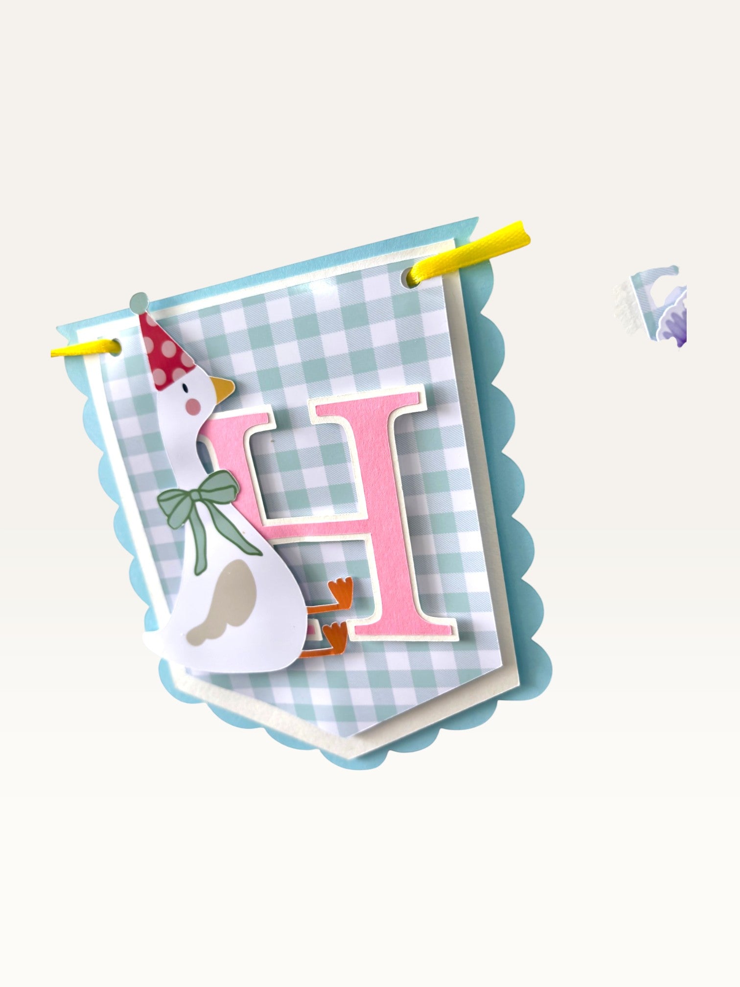Paper Party Studio Gingham Garden birthday banner flag featuring a pink letter H, a goose in a party hat, and blue trim.