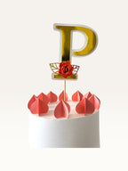 Paper Party Studio personalised gold foil letter P cake topper with a red paper flower and leaf on a wooden pick.