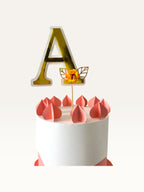 Paper Party Studio personalised gold foil letter A cake topper with an orange paper flower on a white cake