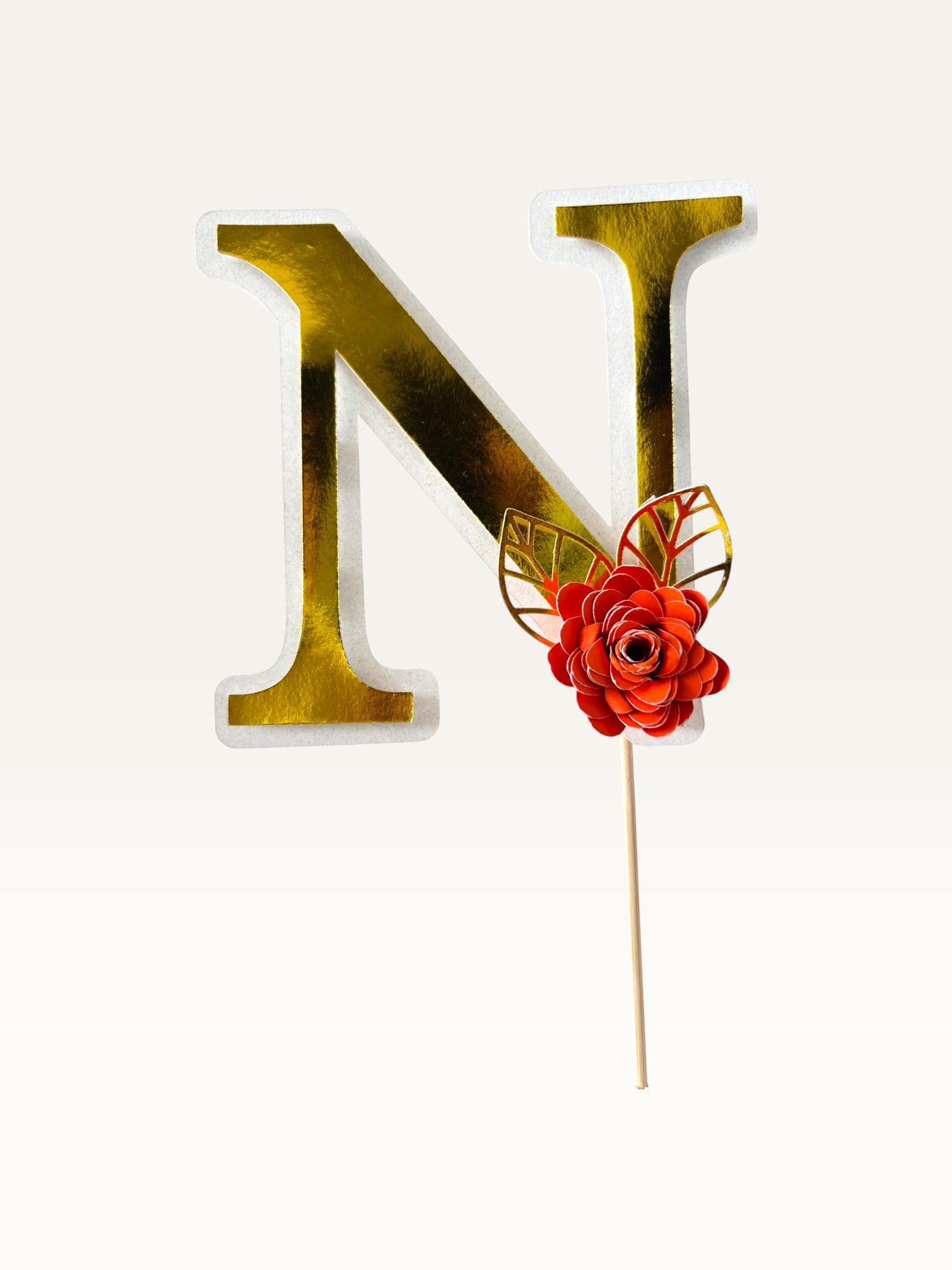 Paper Party Studio personalised gold foil letter N cake topper with a red paper flower and gold foil leaf on a pick.