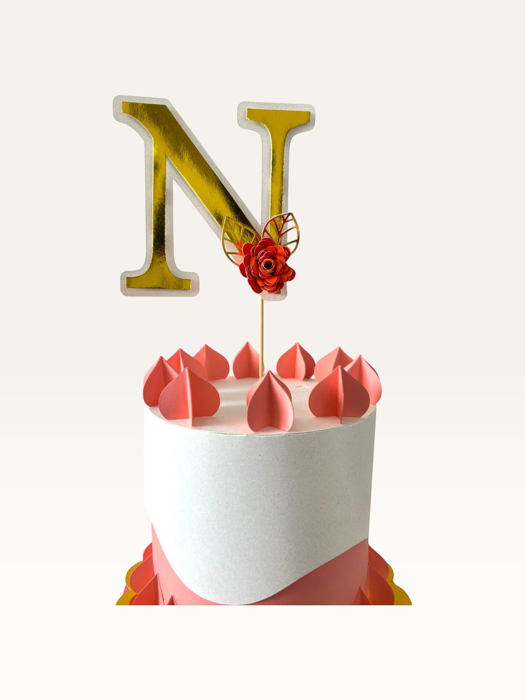 Paper Party Studio gold foil letter N cake topper with a red paper flower and leaf on a wooden pick atop a cake