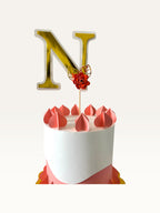 Paper Party Studio gold foil letter N cake topper with a red paper flower and leaf on a wooden pick atop a cake