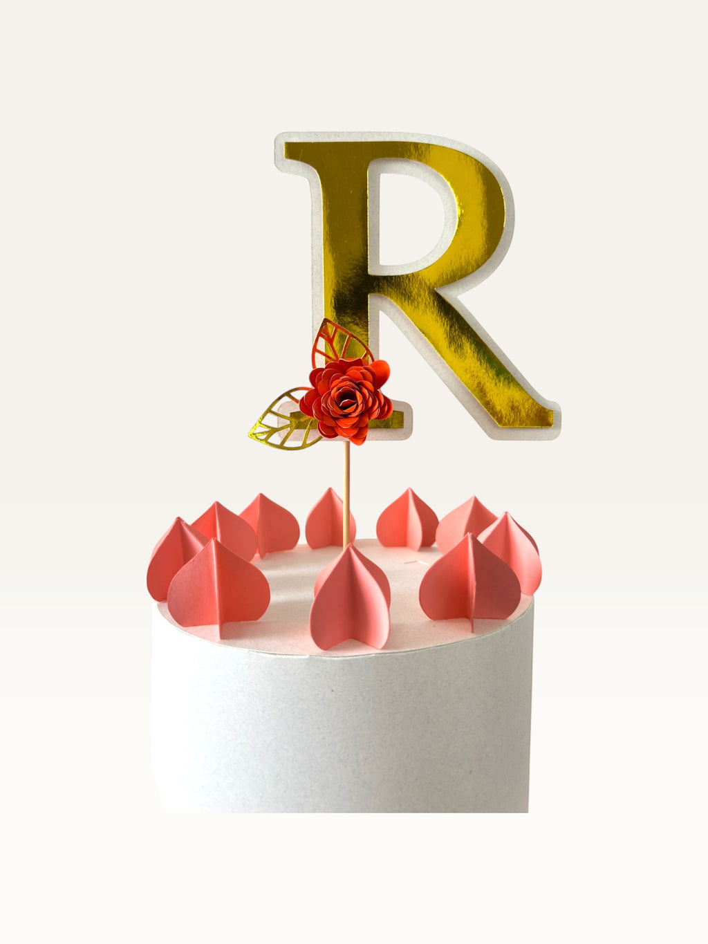 Paper Party Studio personalised gold foil letter R cake topper with a red paper flower and gold leaf on a wooden pick.