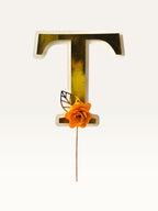 Paper Party Studio personalised gold foil letter T cake topper with an orange paper flower and gold leaf on a pick
