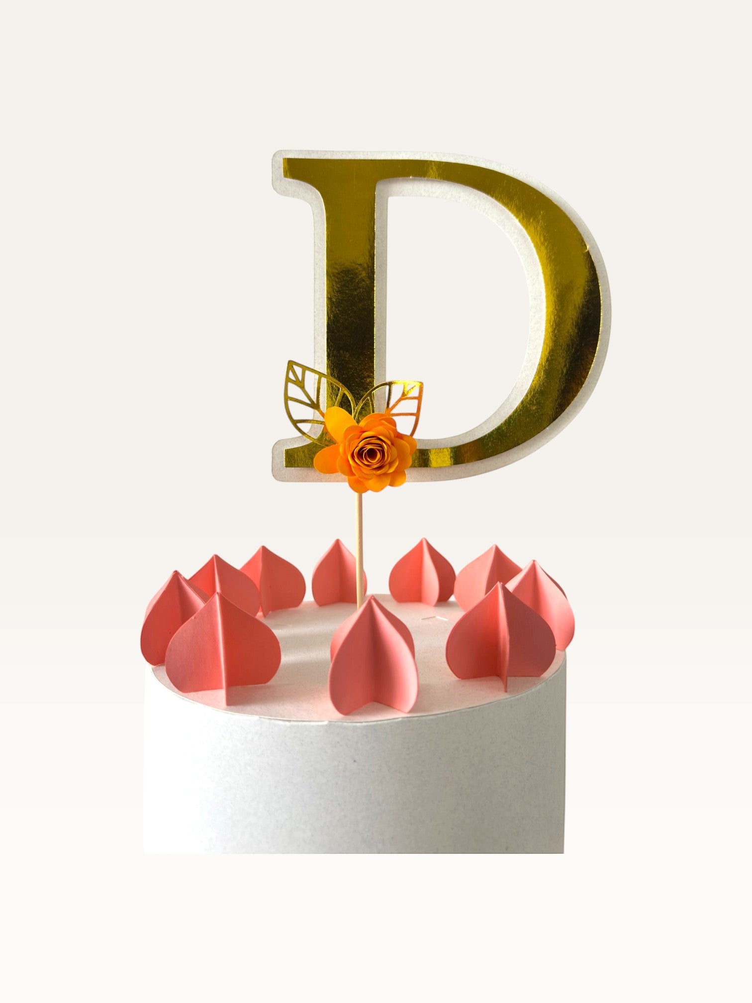 Paper Party Studio gold foil letter D cake topper with an orange paper flower and gold leaf on a wooden pick.