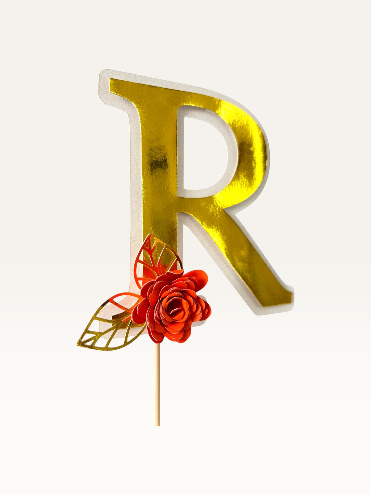 Paper Party Studio personalised gold foil letter R cake topper with a red paper flower and gold foil leaf on a pick