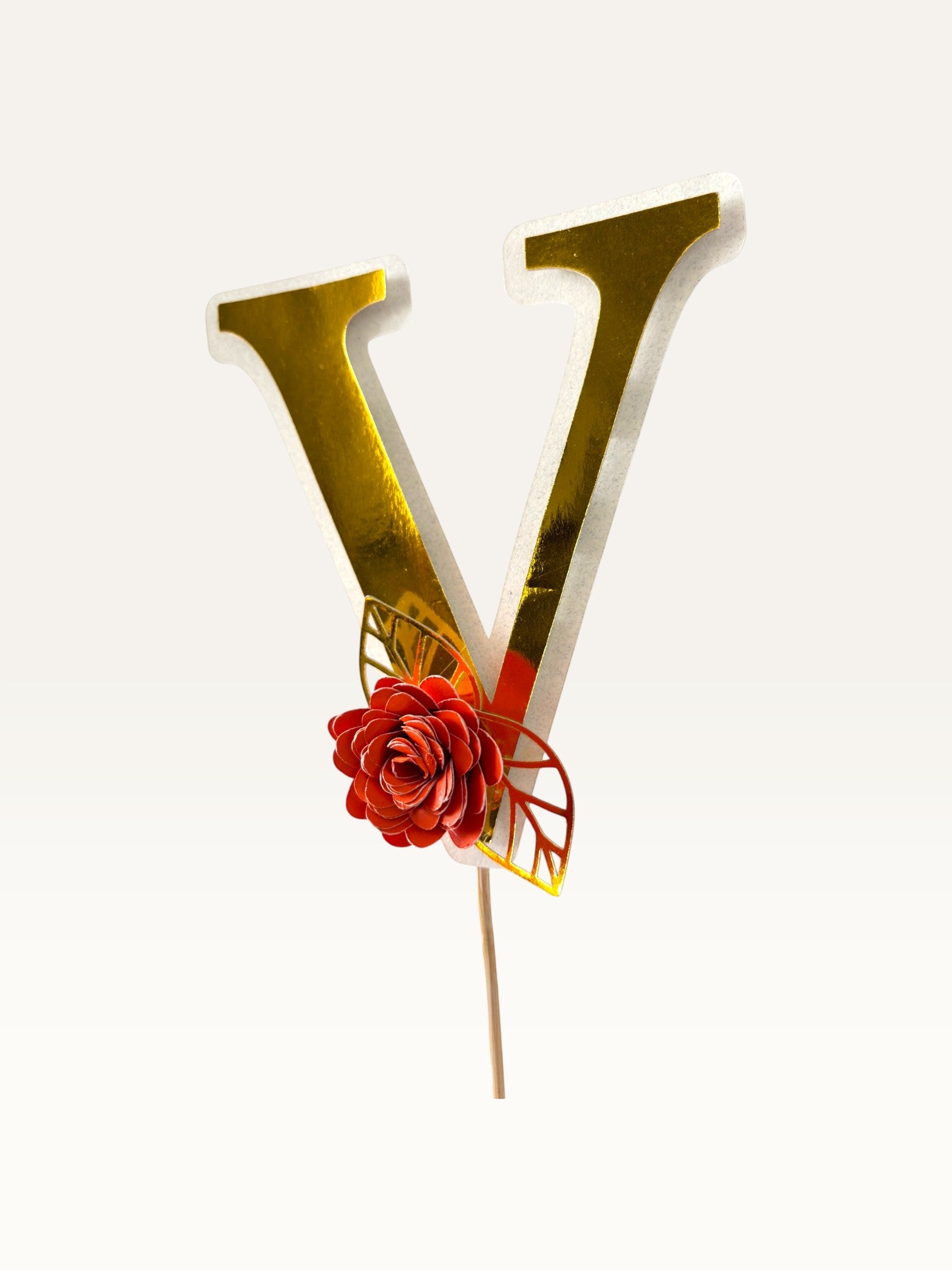 Paper Party Studio personalised gold foil letter V cake topper with a red paper flower and gold foil leaf on a pick