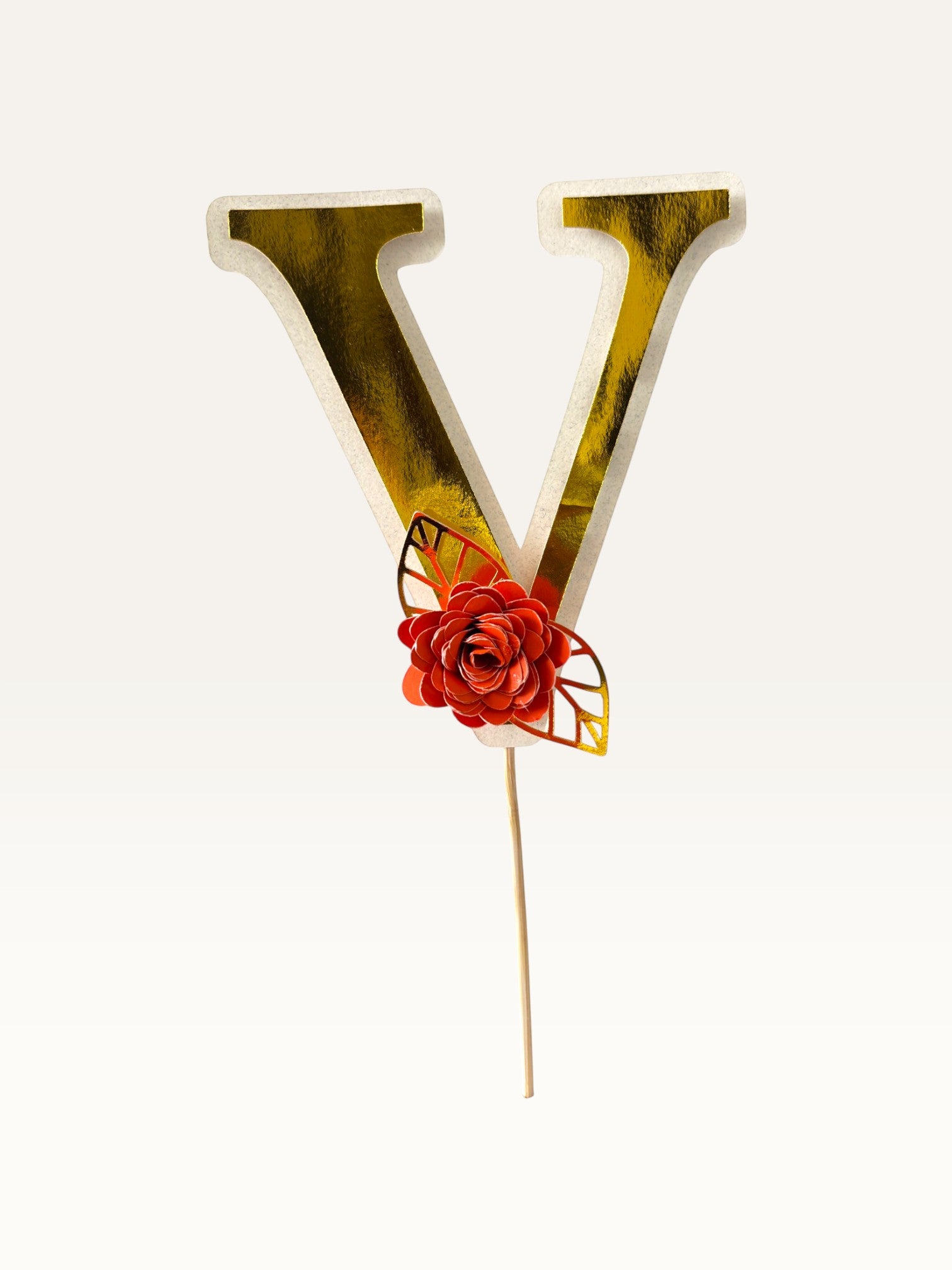Paper Party Studio personalised gold foil letter V cake topper with a red paper flower and gold leaf on a wooden pick