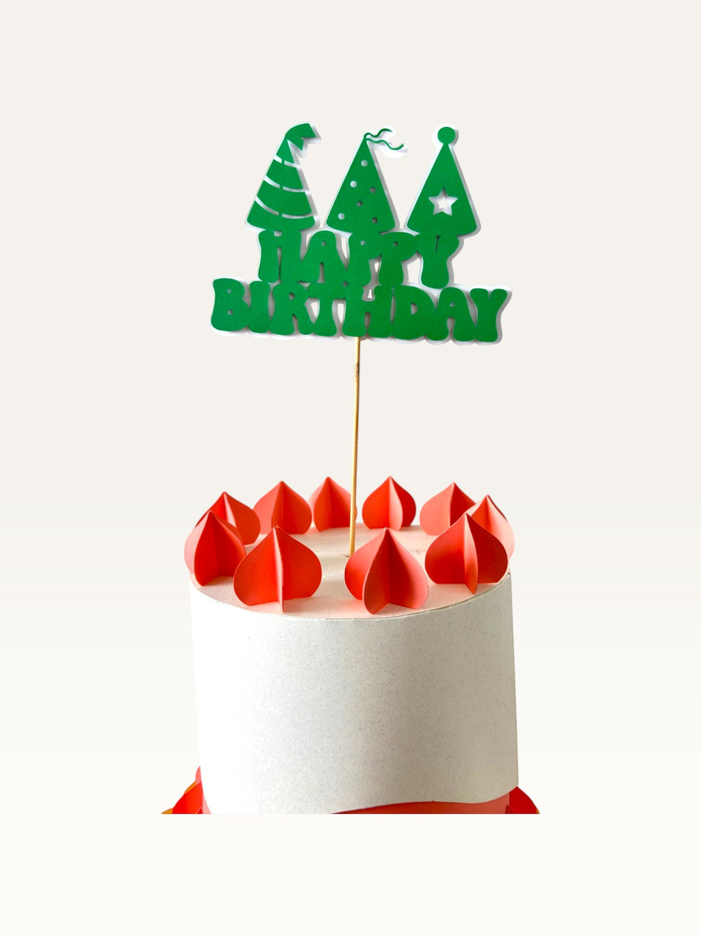 Paper Party Studio green Happy Birthday cake topper with party hat cut-outs on a wooden pick atop a white cake.