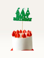 Paper Party Studio green Happy Birthday cake topper with party hat cut-outs on a wooden pick atop a white cake.