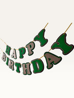 Paper Party Studio layered green and brown Happy Birthday banner with bold cut-out letters on a hanging cord.