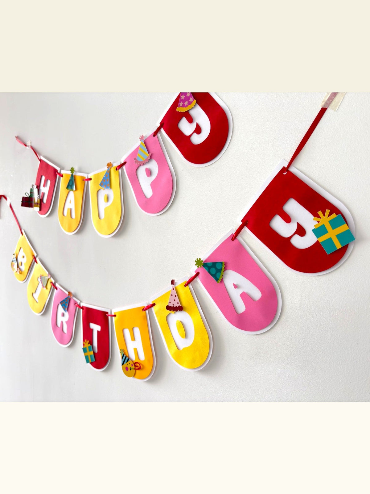 Paper Party Studio Happy Birthday banner with colourful rounded flags, party hats, and gift accents on two strings.