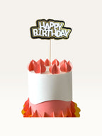 Paper Party Studio layered Happy Birthday cake topper with white lettering, black outline, and gold scalloped backing.