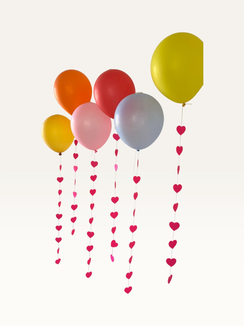Paper Party Studio heart garland strings with pink paper hearts hanging from colorful party balloons